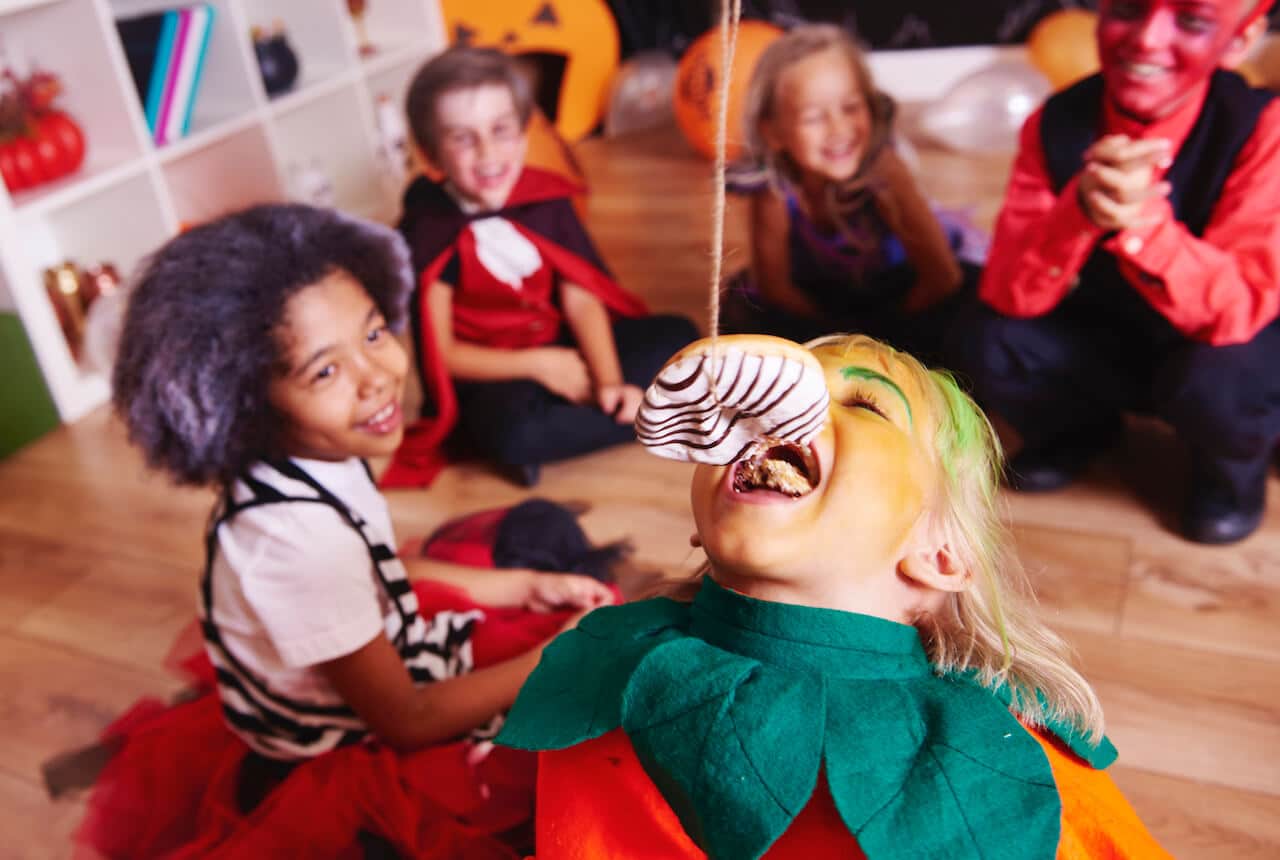 Fasching in Kindergarten und Grundschule: lustiges Spiel: Kind isst ohne Hände Donut von der Schnur