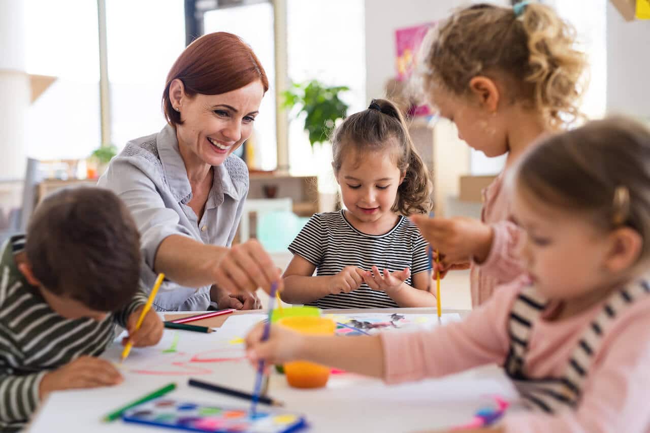 Eingewöhnung Kita - Fazit - Kinder sitzen mit Erzieherin rund um Tisch und basteln.