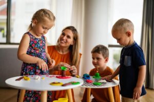 Eingewöhnung in Kita und Kindergarten – Erzieherin spielt mit Kindern an kleinen Tischen.