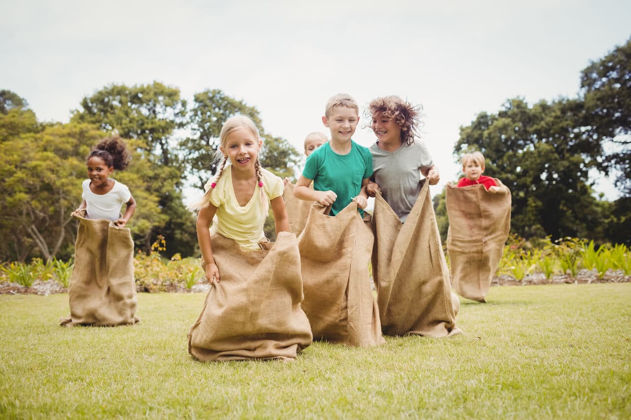 Ostern in Kindergarten und Kita - Eine Gruppe von Kindern spielt auf einer Wiese Sackhüpfen und hat ausgelassen Spaß dabei